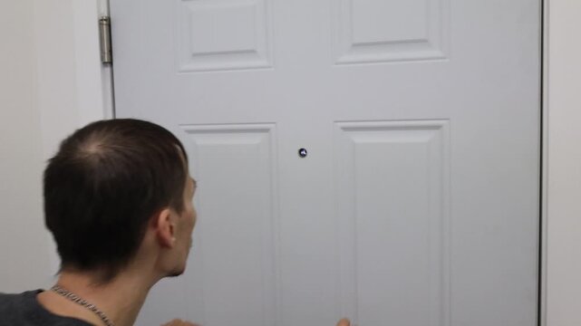 Man checking peephole with hands on door home security fear concept