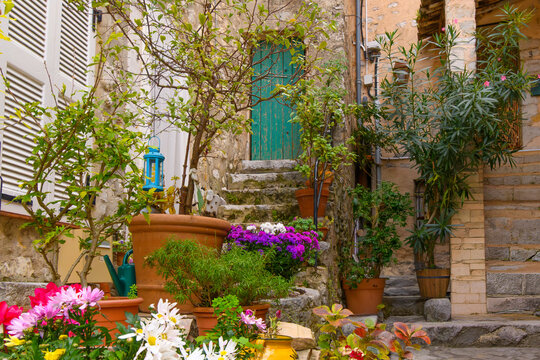 A small courtyard with steps leading to colorful doorways and flowers in the garden in the medieval old town of the village of Gourdon, Alpes-Maritimes, France.