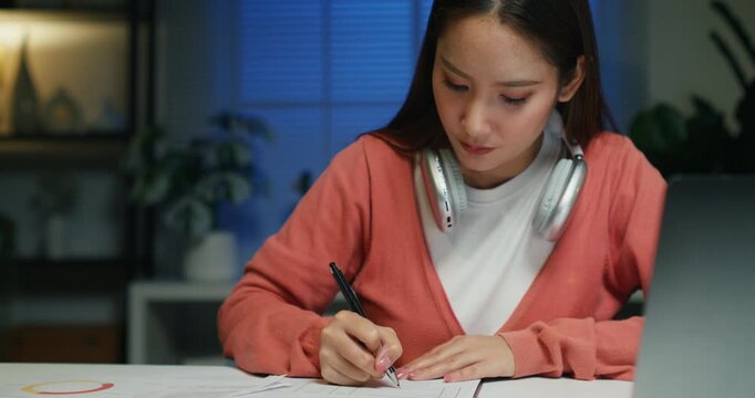 An Asian person inspects tax refund and vat forms, calculating deductions while working late on business financial software.