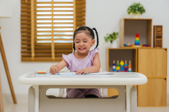 happy preschool child girl drawing and painting with colorful oil pastels on paper