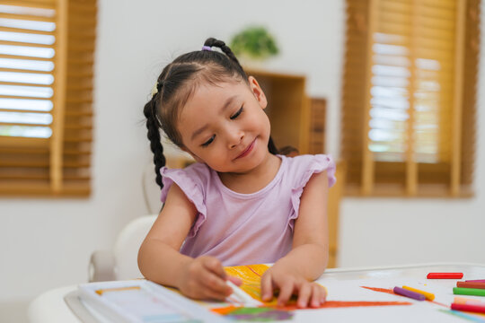 happy preschool child girl drawing and painting with colorful oil pastels on paper