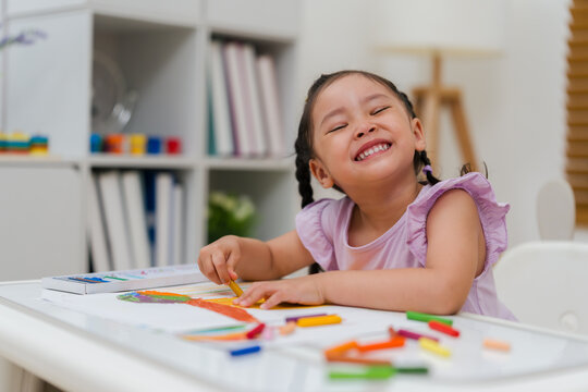 happy preschool child girl drawing and painting with colorful oil pastels on paper