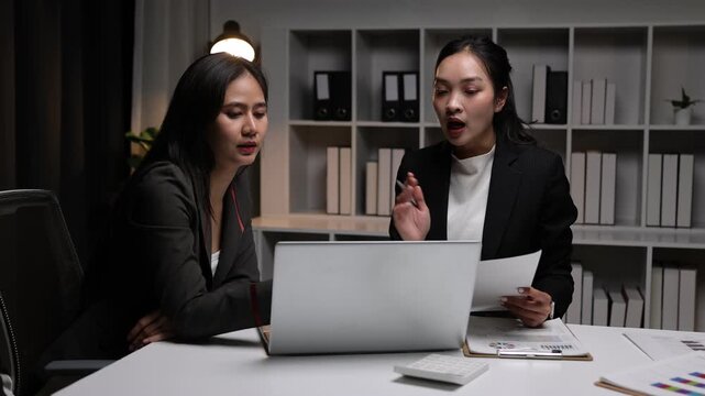 Asian businesswoman arguing about work during late night meeting. Two young businesswomen discussing and arguing over a project in office at night. Colleagues working late to meet a deadline.