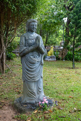 Fototapeta premium A serene Buddha statue stands in prayer, adorned with flowers, symbolizing peace and reflection in Linh Ung Pagoda, Da Nang, Vietnam. The statue is a focal point for meditation.