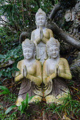 Obraz premium Three praying Buddha statues are displayed in a garden in The Marble Mountains, Da Nang, Vietnam. The statues are a popular tourist destination for those seeking enlightenment.
