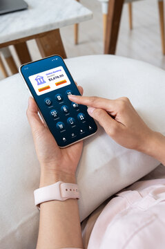 Woman using a smartphone to access online mobile banking. checking balance and making digital transactions at home, showcasing modern fintech and cashless lifestyle.