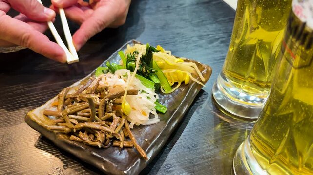 Person Using Chopsticks to Eat Namul Vegetables at Japanese Izakaya