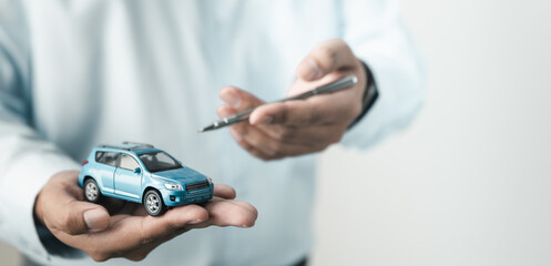 Fototapeta na wymiar Person holding car model while signing agreement, representing vehicle purchase, auto loan, insurance policy and dealership contract process.