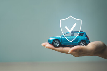 Hand holding a miniature car with protection shield icon, representing car insurance, financial...