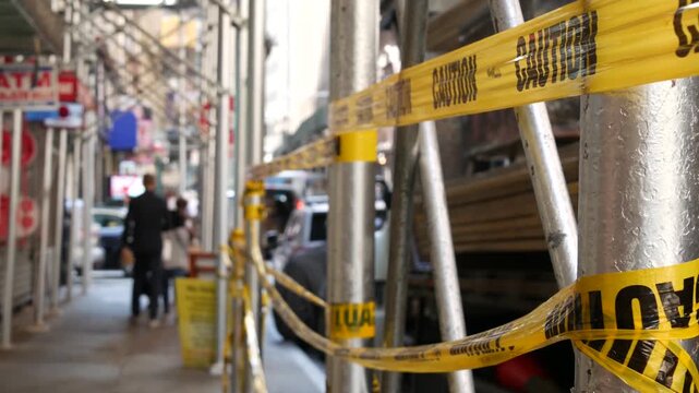 Caution yellow tape and scaffolding on pavement under construction in Manhattan, New York City, United States. Renovation or maintenance, strip barricade or barrier ribbon, scaffold safety warning.