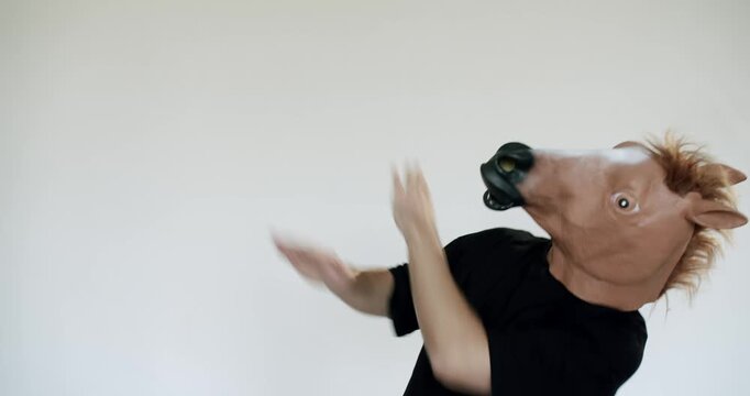 A man wearing a realistic horse mask dances against a minimalist white backdrop. His bizarre performance creates a surreal and humorous atmosphere, perfect for projects needing a touch of the unusual.