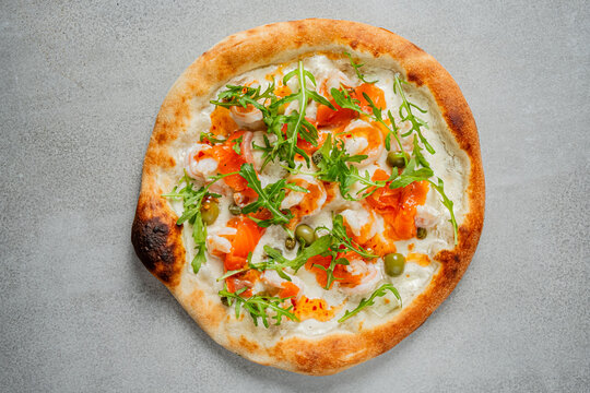 Savory pizza topped with fresh salmon, arugula, and olives on a rustic table setting