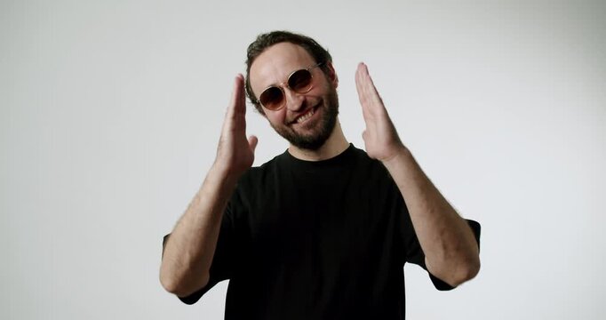 Happy man in sunglasses smiles and claps his hands. Joyful person on a white background. He smiles and expresses positive emotions of happiness and joy. Perfect for lifestyle and advertising projects.
