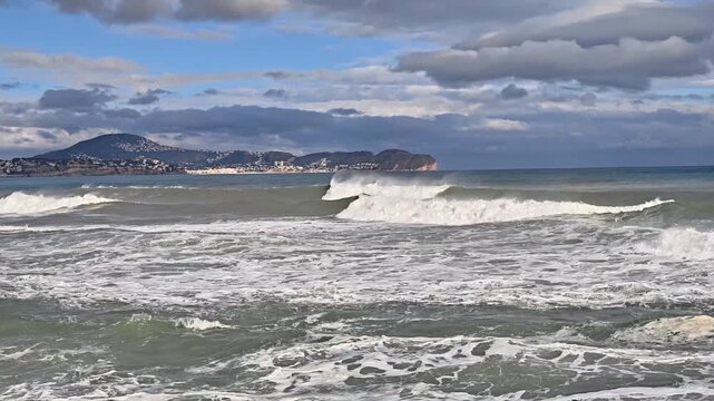 stormy ocean waves crashing near headland, dramatic clouds, distant island, powerful surf and foamy breakers