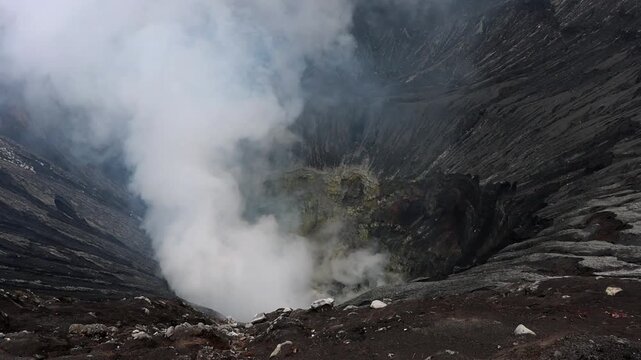 Dramatic view inside the crater of Mount Bromo volcano of thick white volcanic steam rises from active vents deep within the crater basin in in East Java, Indonesia