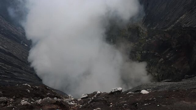 Close view inside the crater of Mount Bromo volcano, where thick white volcanic steam and gases rise intensely from active vents deep within the crater in East Java, Indonesia