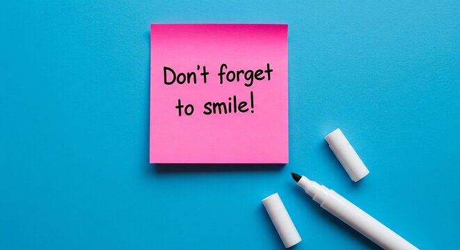 A pink note with a reminder to smile on a blue surface with a white marker
