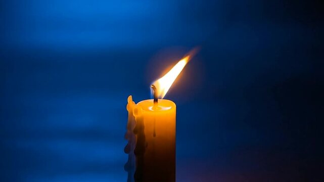 A single yellow candle burns brightly with a warm flame against a dark blue background, with melted wax dripping down its side.
