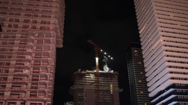 Active construction at night between high rise buildings with crane and lights showing nonstop urban development progress technology and modern city expansion