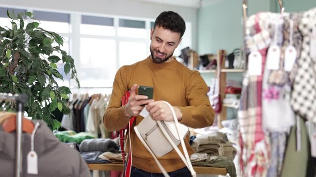 Young man buyer scanning qr code for women's handbag in clothing store 