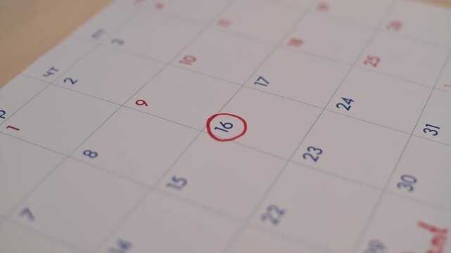 A hand marks the date on a calendar with a red marker, indicating an important day for planning.