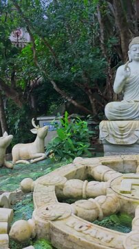 A serene Buddha statue sits among deer sculptures and a Dharma wheel in the gardens of The Marble Mountains, in DA NANG, Vietnam. The statues symbolize peace and harmony.