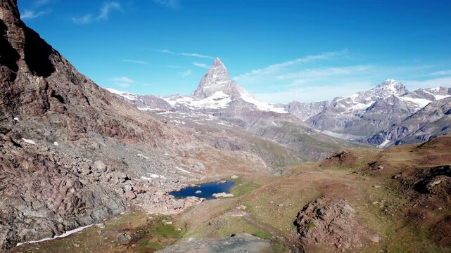 Iconic Matterhorn peak rising above an alpine valley, rocky terrain and small mountain lakes under a clear blue sky, showcasing classic Swiss Alps scenery