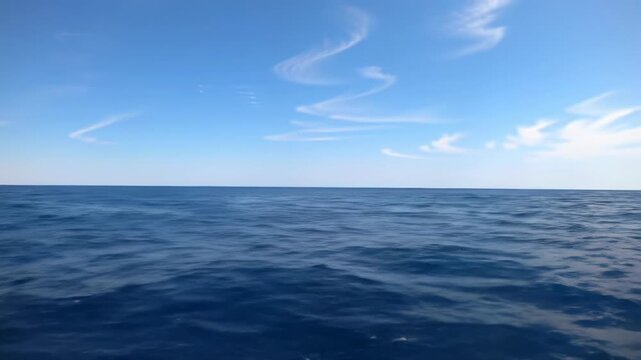A serene wide video of a deep blue ocean with gentle, rippling waves and white crests under a vast azure sky with wispy clouds, camera dolly video forward. Profound sense of calm and tranquility