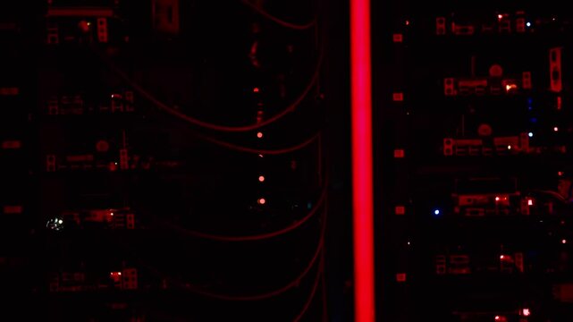 Rack servers and optical fiber cables in modern data center with red light and dust particles.