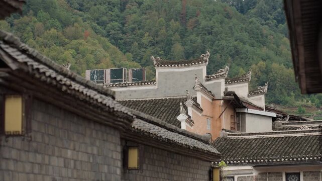 Stone rooftops and narrow alley, mountain backdrop detailed view of tiled eaves and weathered brick, lantern glow, subtle solar panels, muted foliage, contemplative heritage mood