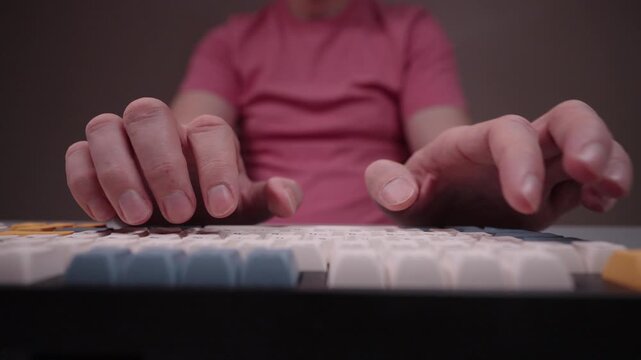 Low-angle view of male fingers typing on custom mechanical keyboard with colorful keycaps. Close-up hands of unrecognizable programmer, journalist, gamer working on computer. Shooting in slow motion.