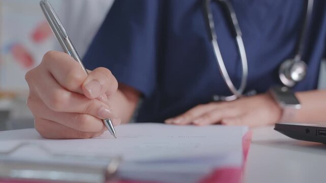 A female doctor note in book at a white wooden desk in her hospital office. The image shows a close-up of her hands, illustrating diagnoses and recording patient symptoms.