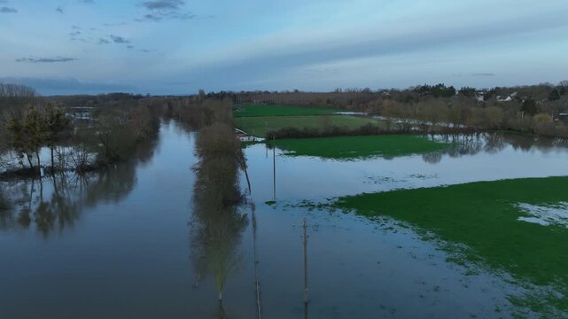 Aerial view of flooded fields and trees in Sarthe department at dusk with calm brown water reflecting the evening sky