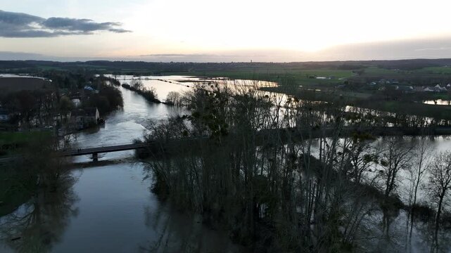 Aerial view of flooded river with bridge in Sarthe department at sunset showing calm water trees and distant houses with golden light reflection