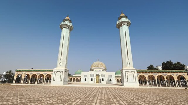 Scenic general view of sun-drenched Mausoleum of Habib Bourguiba in Tunisian city of Monastir, showcasing exquisite Islamic architecture with golden dome and twin white minarets. High quality 4k