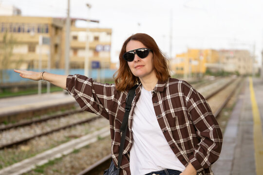 woman stopping train at railway station platform looking away reaching out arm wearing plaid shirt on urban background concept of travel, transportation, commuting