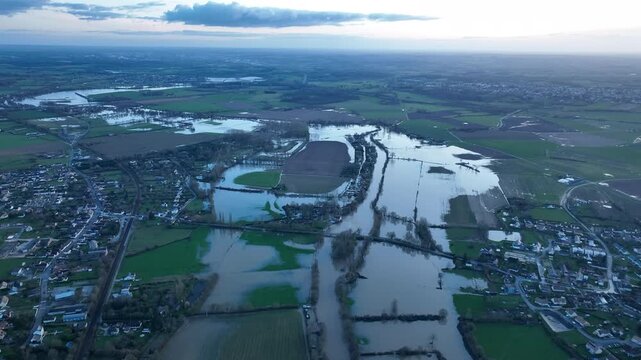 Aerial panorama of severe flooding across Sarthe department showing vast brown water covering fields roads and surrounding a town under cloudy sky