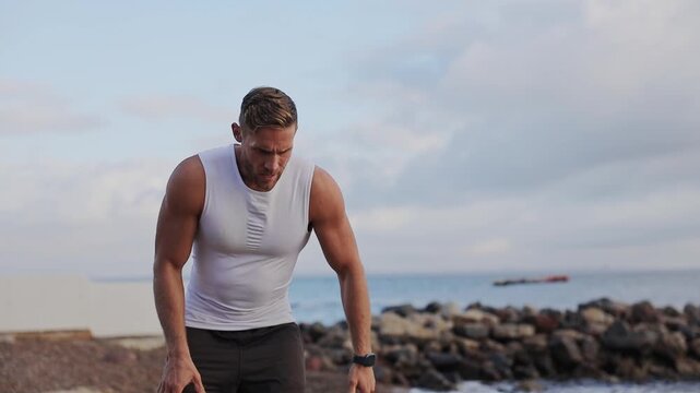 Young strong toned sporty athletic fit sportsman man wear sports clothes run sweating take respite break warm up train at sunrise sun dawn over sea beach outdoor on pier seaside in summer day morning