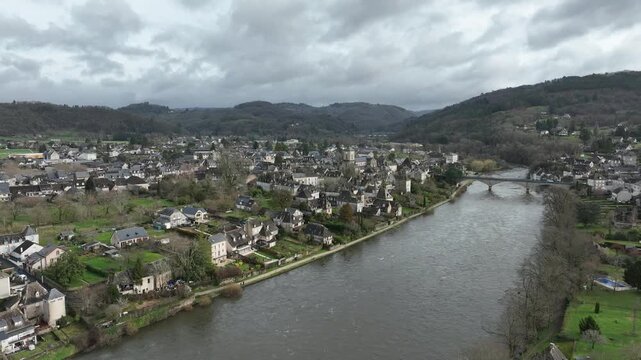 Aerial view of Argentat sur Dordogne with historic town buildings along the Dordogne river and stone bridge under cloudy sky