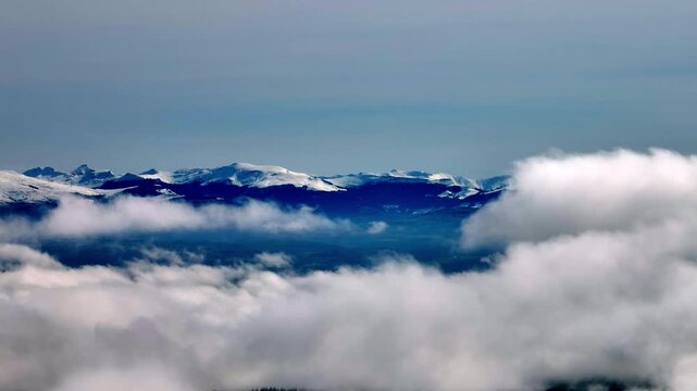 Aerial view above the clouds of snow-capped mountains in Correze under bright blue sky with dramatic cloud formations