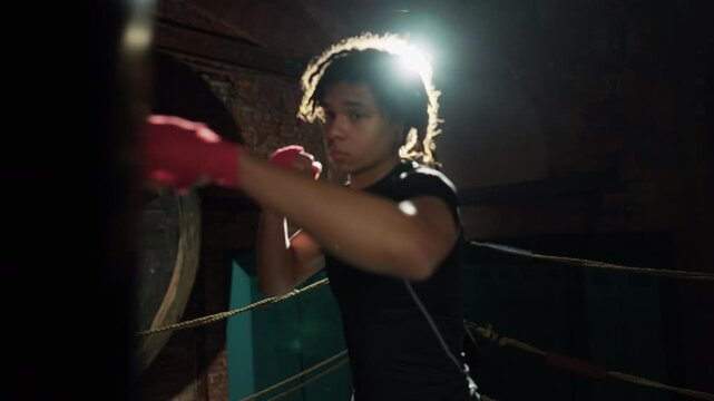 Motivated box fighter training alone, striking punch bag by arms, portrait. Professional sportsman practicing in gym, preparing to competition and championship, sportive hobby and self-defense class
