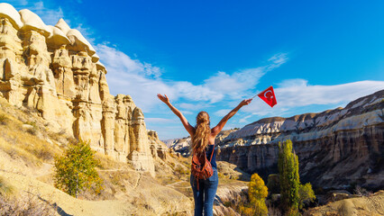 Obraz premium Young Woman Hiker Celebrating with Turkish Flag Overlooking Cappadocia Fairy Chimneys Landscape