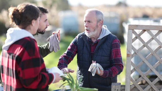 On bright spring day, middle-aged couple swear with senior man neighbor. Squabbles between neighbors, debates or misunderstandings, territorial dispute.