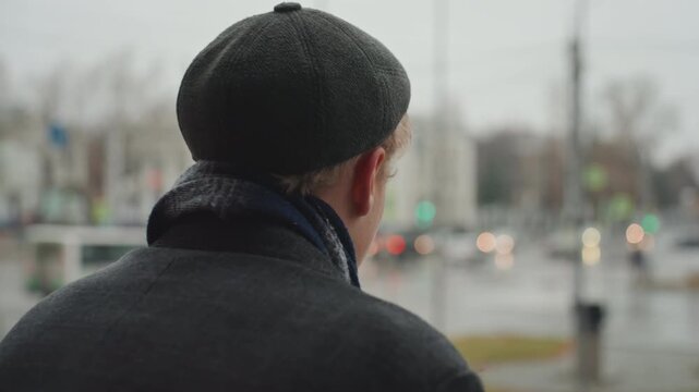 Moody urban portrait white creator glancing over shoulder on rainy city balcony, wet hair under wool cap, scarf and coat flecked with sleet, shallow depth of field, traffic bokeh and muted cinematic