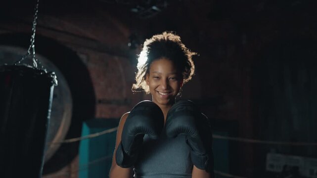 Joyful athletic woman smiling to camera in boxing ring, young female box fighter . Medium portrait of african american sportswoman in fight club, do combat sport for good body shape and self-defense