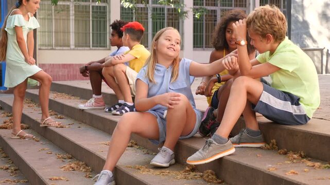 Group of kids sitting on stairs outdoors and talking. Boy and girls having conversation.