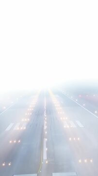 Vertical pov of airplane landing on runway in heavy fog with atmospheric glowing lights in Milan, Italy