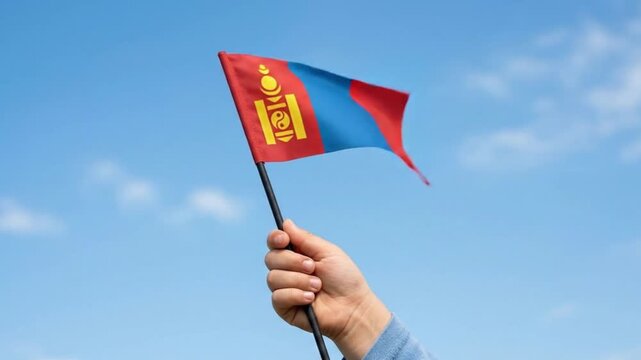 Hand Holding and Waving Small Mongolia Flag Against Blue Sky Background