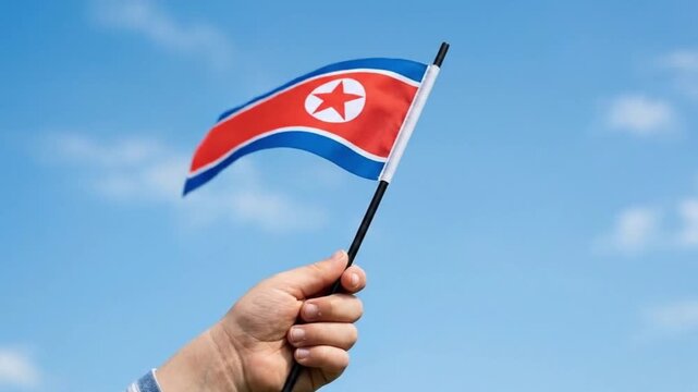 Hand Holding North Korea Flag Waving against Blue Sky