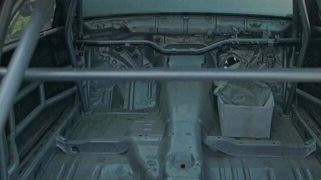 A smooth cinematic pan across the bare metal interior of a stripped-down race car, showing the custom roll cage and industrial chassis under soft garage lighting.